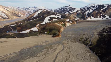 The-orbit-flight-over-a-wide-glacier-riverbed-in-the-mountains-of-Landmannalaugar-covered-by-patches-of-snow-in-Iceland