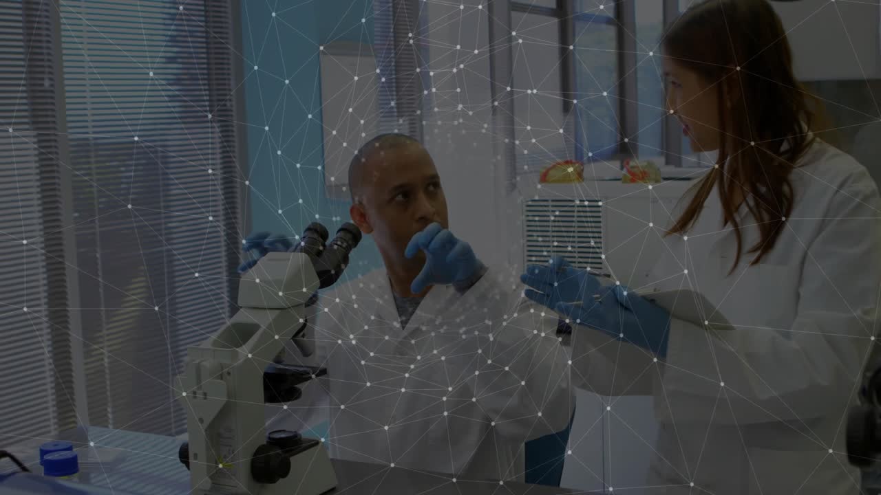 Laboratuvar lamını inceleyen erkek bilim insanının yanına flakonla giren meslektaş, tablete dokunarak boyutu açıklıyor.