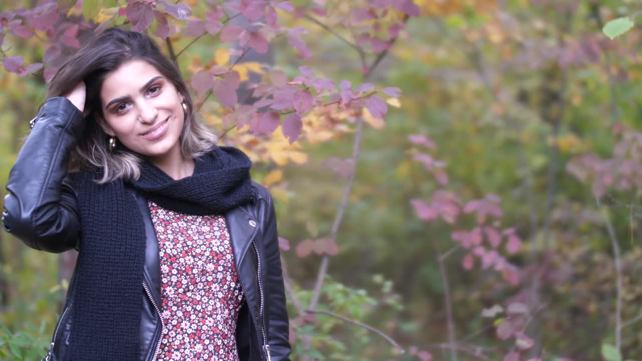 Brunette i høstskog står nær gule og røde blader og smiler inn i kameraet.