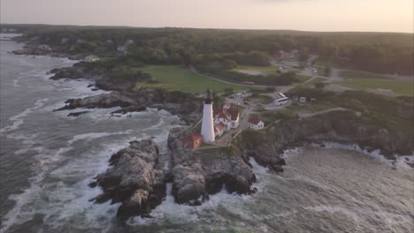 aerial shot looking down at the portland head light lighthouse on a rocky point in the atlantic ocean with waves crashing against the shore