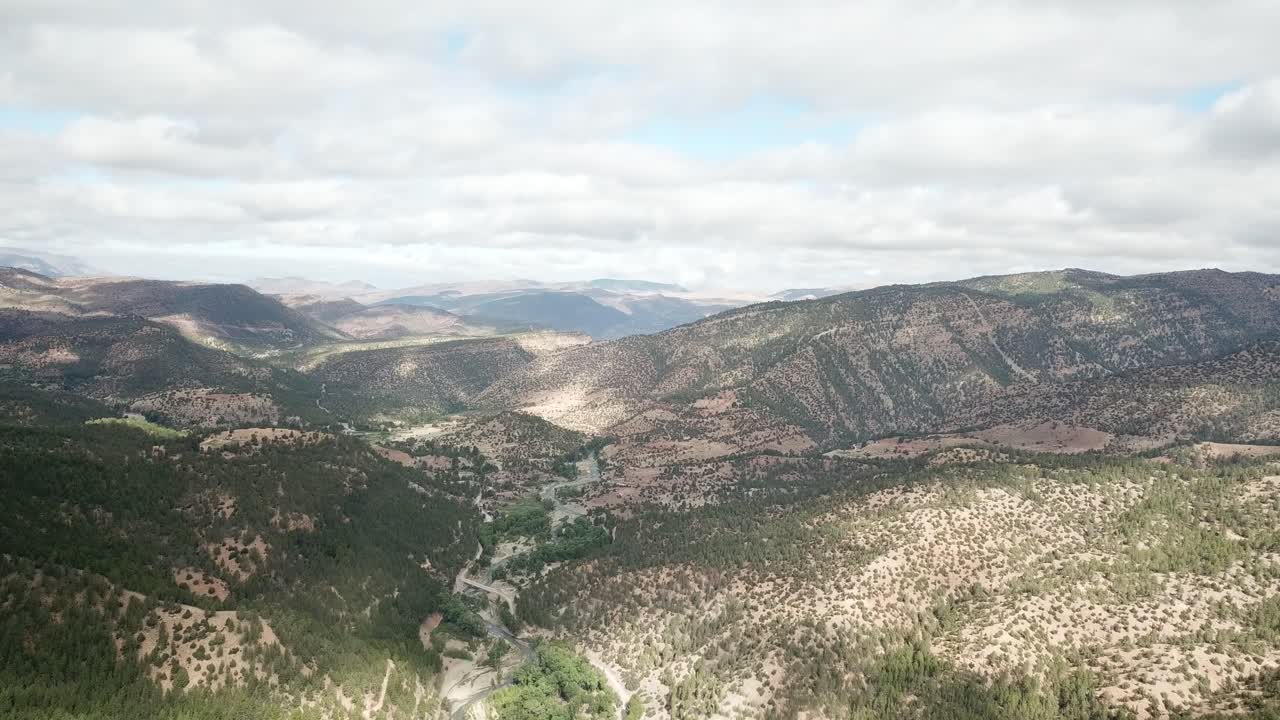 Drone footage captures Morocco's towering Atlas peaks piercing azure skies, their snow-capped summits casting dramatic shadows across rugged ridges and deep valleys below