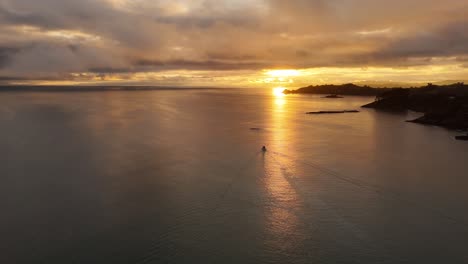 aerial panorama of boat cruising on sea during golden sunset. mystic clouds at sky. coastline of waiheke island, new zealand.