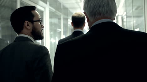 bearded businessman walks through a hallway together with an older gray haired colleague