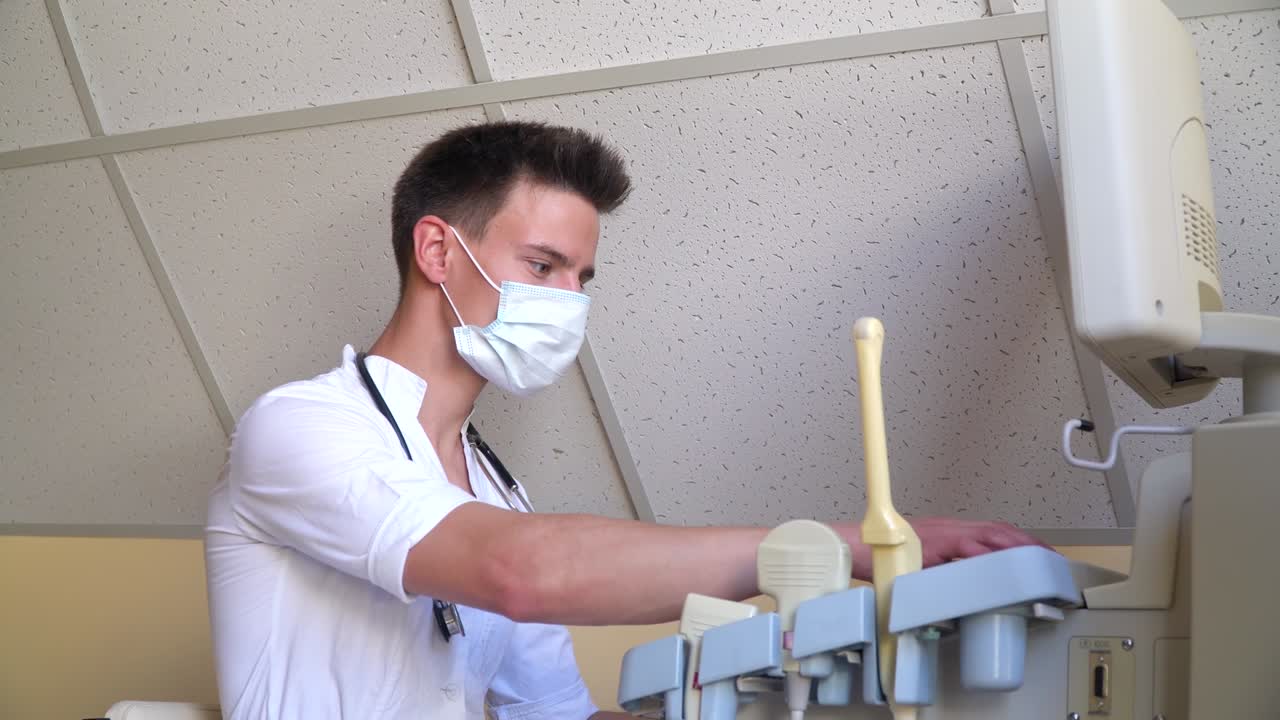 Young doctor in protective mask working on ultrasound device. Diagnostics covid 19