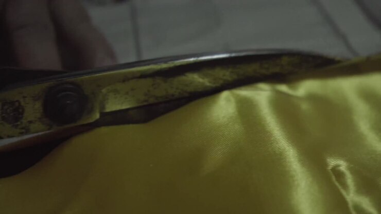 Old lady tailor use scissors to cut yellow fabric