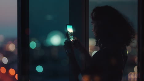 happy business woman using smartphone taking photo of city at night enjoying beautiful view working late in office