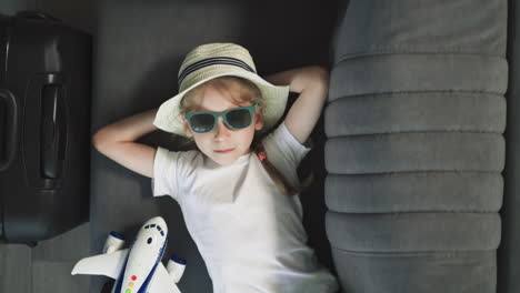 small girl in hat with hands behind head relaxes at home