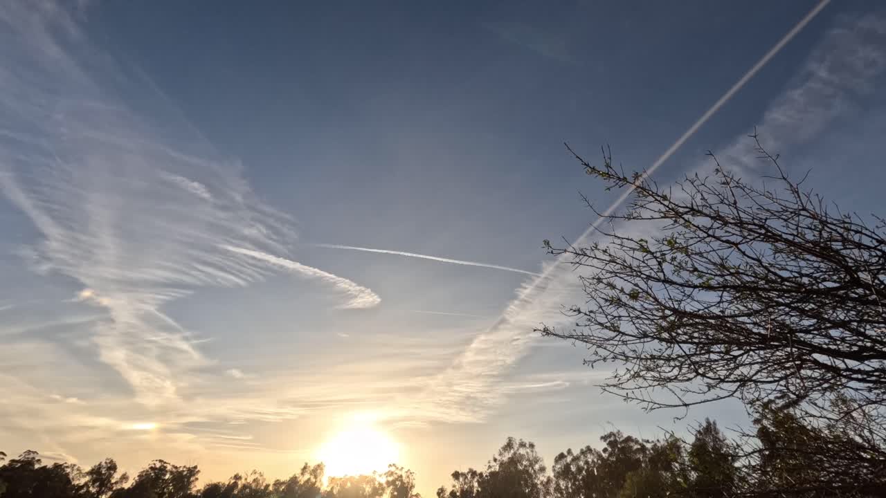 Breathtaking golden hour sunset across a forested horizon with sun rays cutting through sparse clouds in a wide cinematic frame.