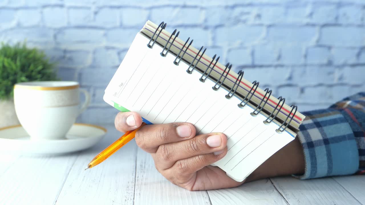 Hand holding a spiral notebook with pen