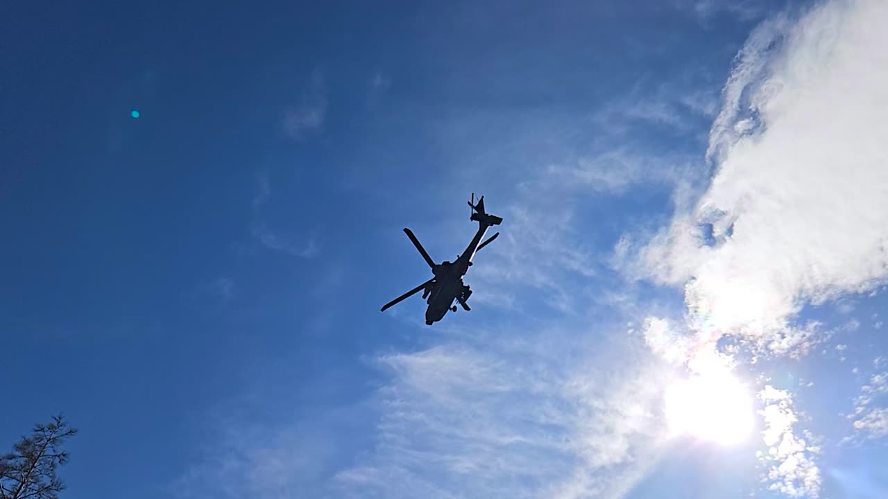 Rare slow motion footage of a United States military army Apache AH-64 helicopter flying over a battlefield with trenches during a sunny summer day in a pine forest in the Baltics europe. Silhouette.
