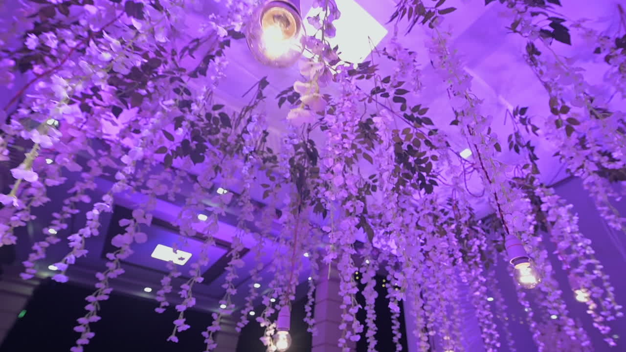 A dreamy Indian wedding reception decor with purple lights and floral ceiling. Slow motion.