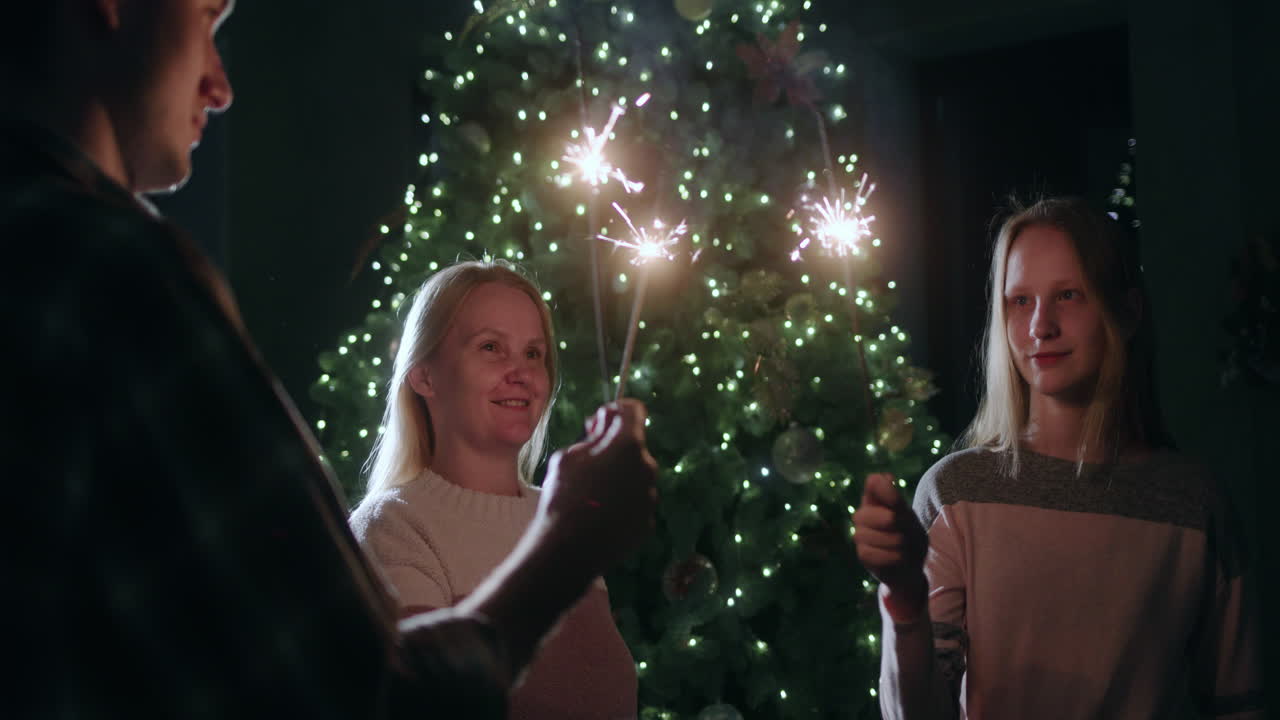 Una famiglia felice festeggia il nuovo anno all'albero di Natale, tenendo in mano stelle filanti accese