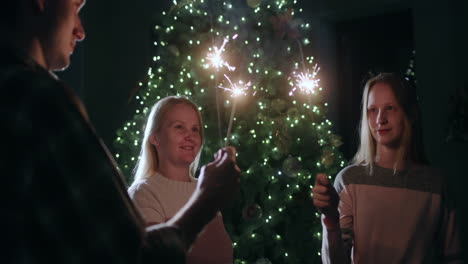 a happy family celebrates the new year at the christmas tree, holding burning sparklers