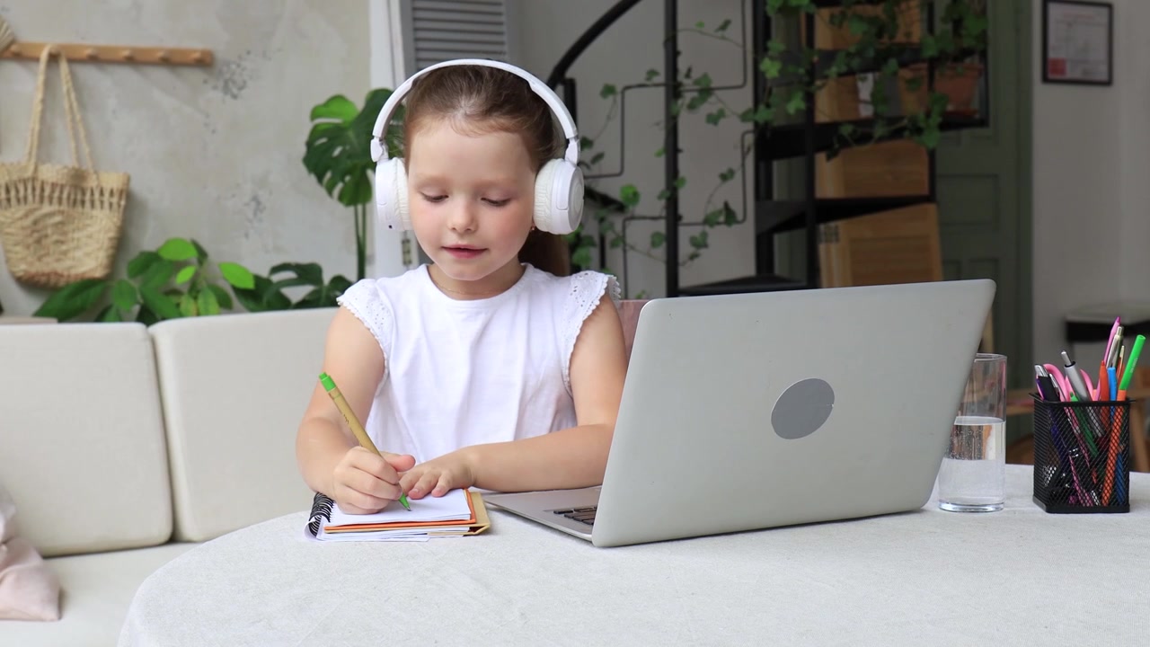 Young Girl with Headphones Studying Online Using Laptop at Home