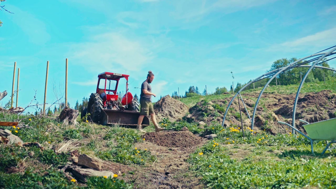 A man operates a red tractor while working on a farm field in the Norwegian countryside - timelapse