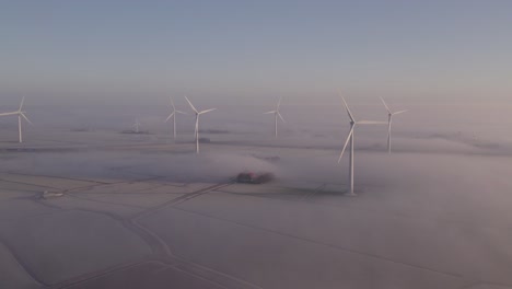 Spinning-wind-turbines-during-a-foggy-morning-at-dutch-countryside,-aerial