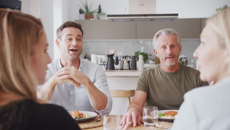 family with senior parents and adult offspring eating meal around table at home together
