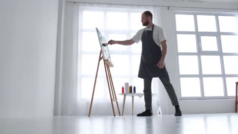 the artist paints an abstract picture he is focused on work painting on an easel in his art studio - the artist paints an abstract picture, he is focused on work, painting on an easel in his art studio, creative atmosphere