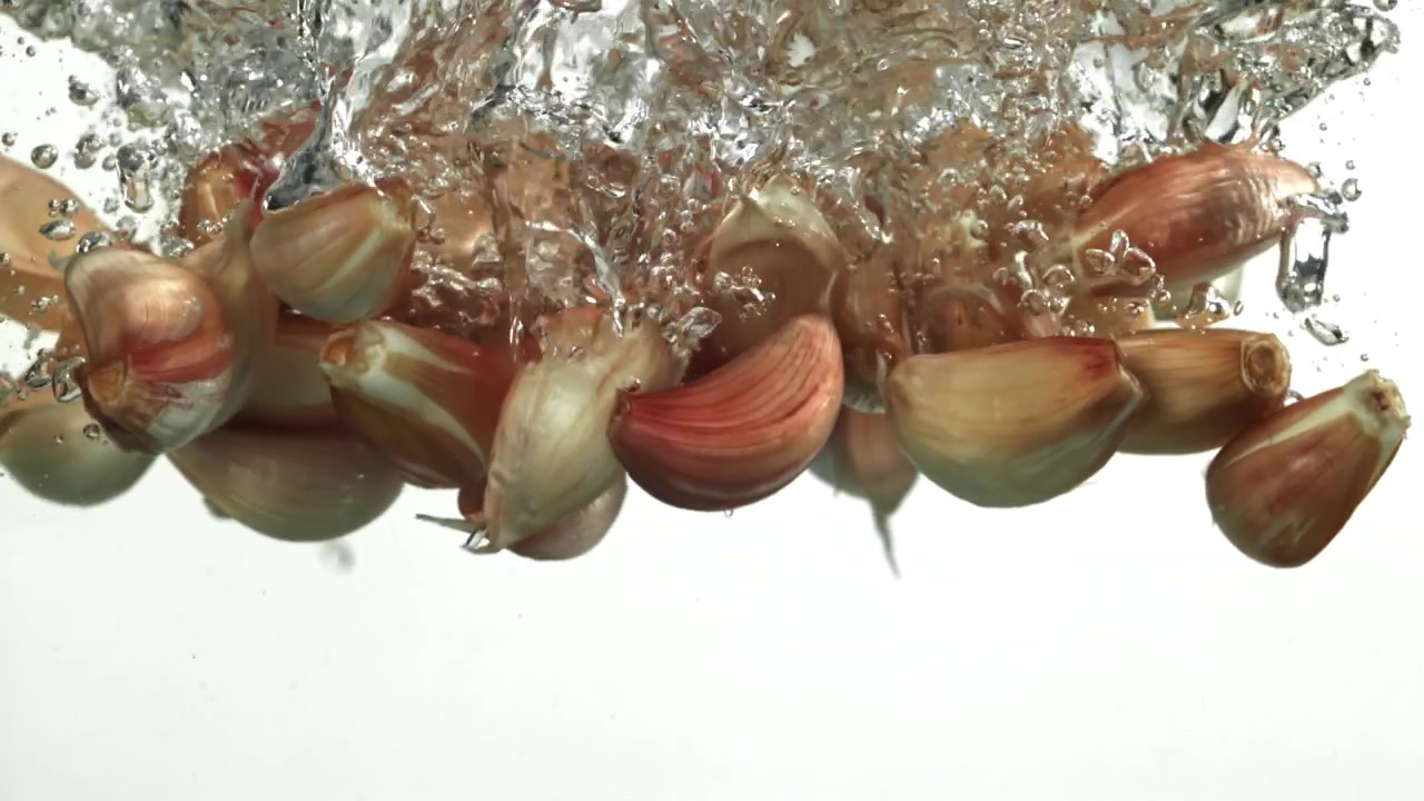 Garlic Cloves Falling into Water with Bubbles on White Background