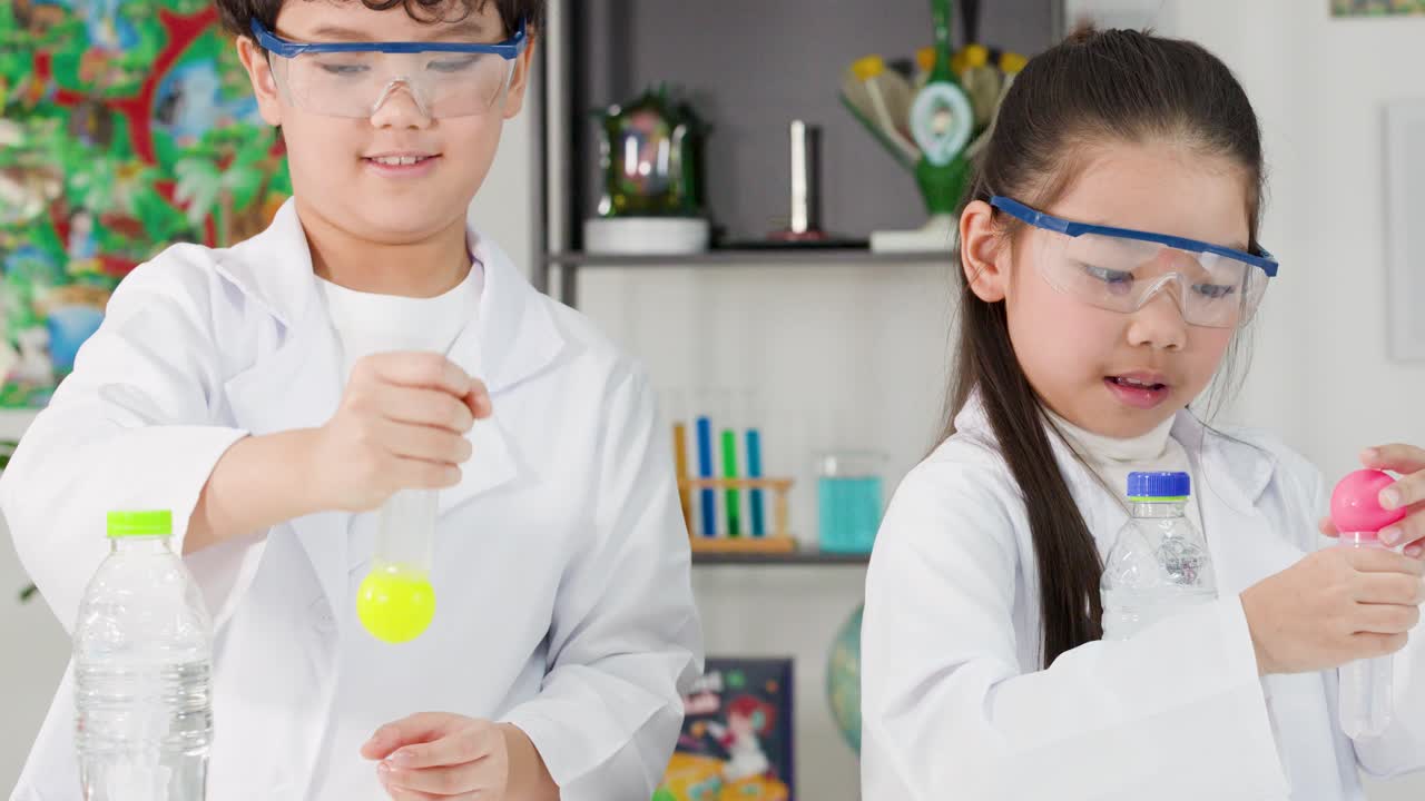 Dua anak Asia berjas lab melakukan eksperimen fisika menggunakan botol dan bola pingpong