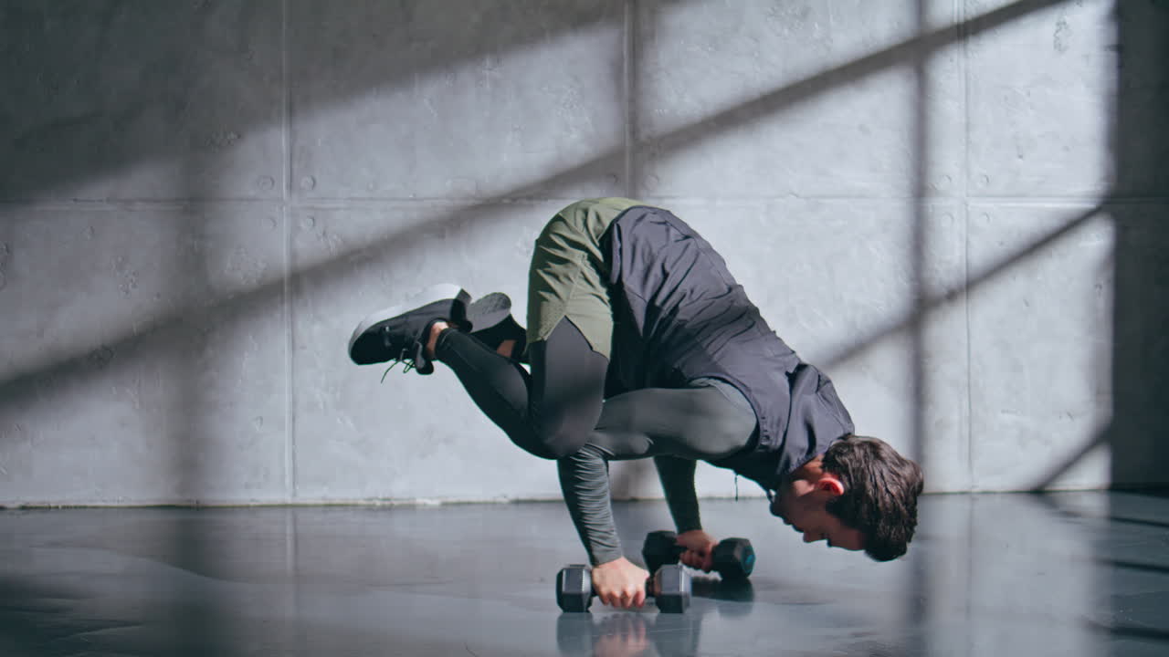 Strong man exercising dumbbells standing on hands in gym. Guy using weights