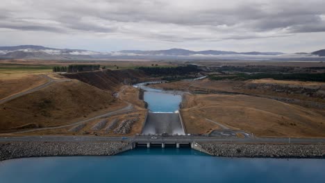 cars driving over dam of blue, alpine lake in new zealand