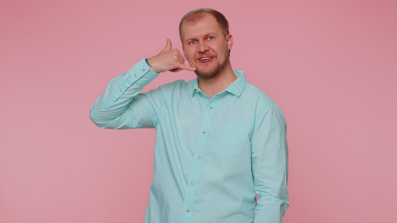 alegre un hombre con camisa azul mirando a la cámara haciendo un gesto de teléfono como dice hola me llamas