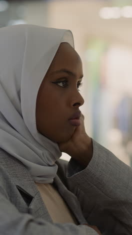 unhappy african-american woman with chiffon hijab leans on shopping gallery handrail in trade mall closeup. muslim lady with bad thoughts. mental state