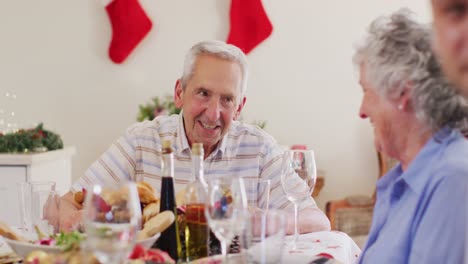 Caucasian-senior-man-talking-while-sitting-on-dining-table-enjoying-lunch-together-during-christmas-