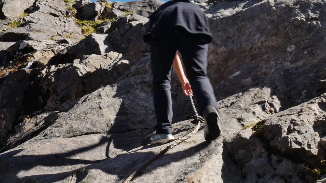 hiker climbs rock face with steel cable