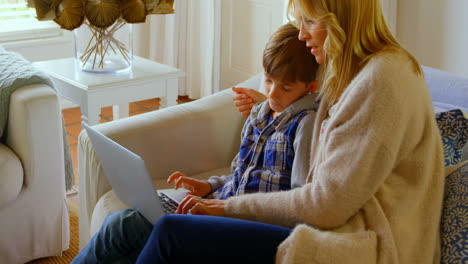 Vista-Lateral-De-Una-Joven-Madre-Caucásica-Enseñando-A-Su-Hijo-Usando-Una-Computadora-Portátil-En-Un-Hogar-Cómodo-4k