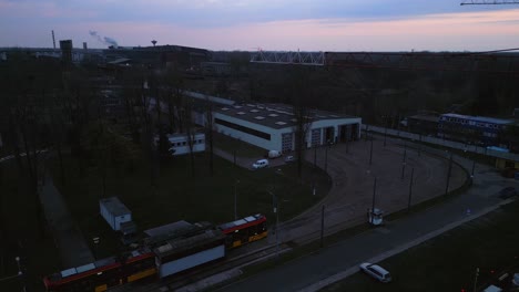 Una-Toma-Aérea-De-Un-Tranvía-Que-Llega-A-Una-Parada-Para-Su-Inspección,-Con-Una-Fundición-De-Metal-En-El-Fondo-Durante-La-Puesta-De-Sol