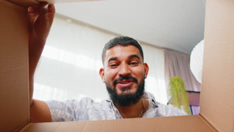 happy indian man shopper unpacking cardboard box delivery parcel online shopping purchase at home