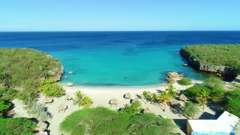 hidden caribbean sandy beach cove bay with beachside huts at daaibooi beach in curacao, aerial