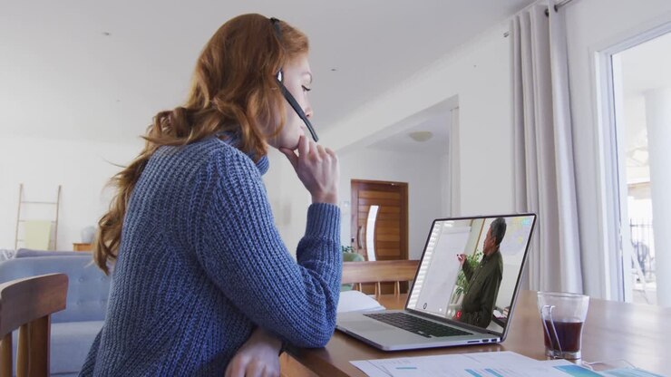Studentessa caucasica che usa un laptop e delle cuffie con microfono in videochiamata con un insegnante uomo