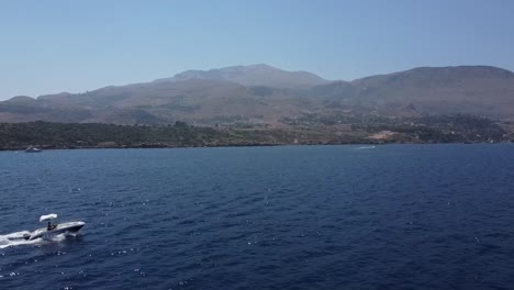 Lancha-Rápida-Navegando-En-El-Mar-Azul-Profundo-Con-Paisaje-De-Montaña-En-El-Fondo-En-Scopello,-Trapani-En-Sicilia,-Italia