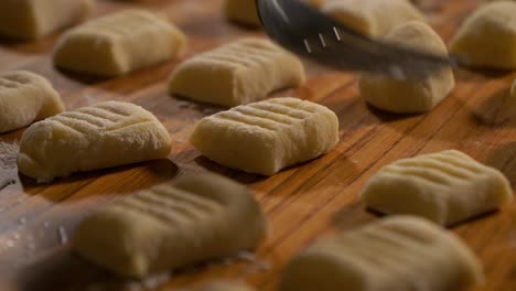 4k close up shot pressing homemade fresh raw gnocchi on the top with a silver fork on a wooden table