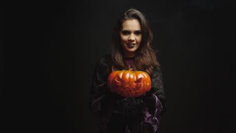 Young-woman-dressed-up-like-a-witch-holding-a-pumpking