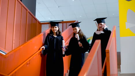 Tres-Felices-Estudiantes-De-Preescolar-Con-Toga-Y-Birrete-Corriendo-Por-Las-Escaleras-Y-Sosteniendo-Un-Diploma-En-La-Ceremonia-De-Graduación