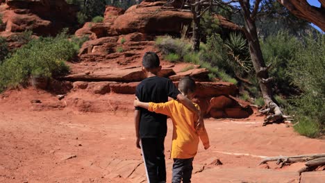 a native american indian boy and his brother walk arm in arm near some red rock buttes in sedona arizona