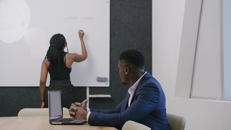 Femme africaine écrivant "création de contenu" sur un tableau blanc, réfléchissant à des idées et élaborant des stratégies dans un environnement professionnel créatif