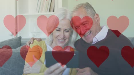 Animation-of-social-media-heart-icons-over-senior-couple-using-smartphone