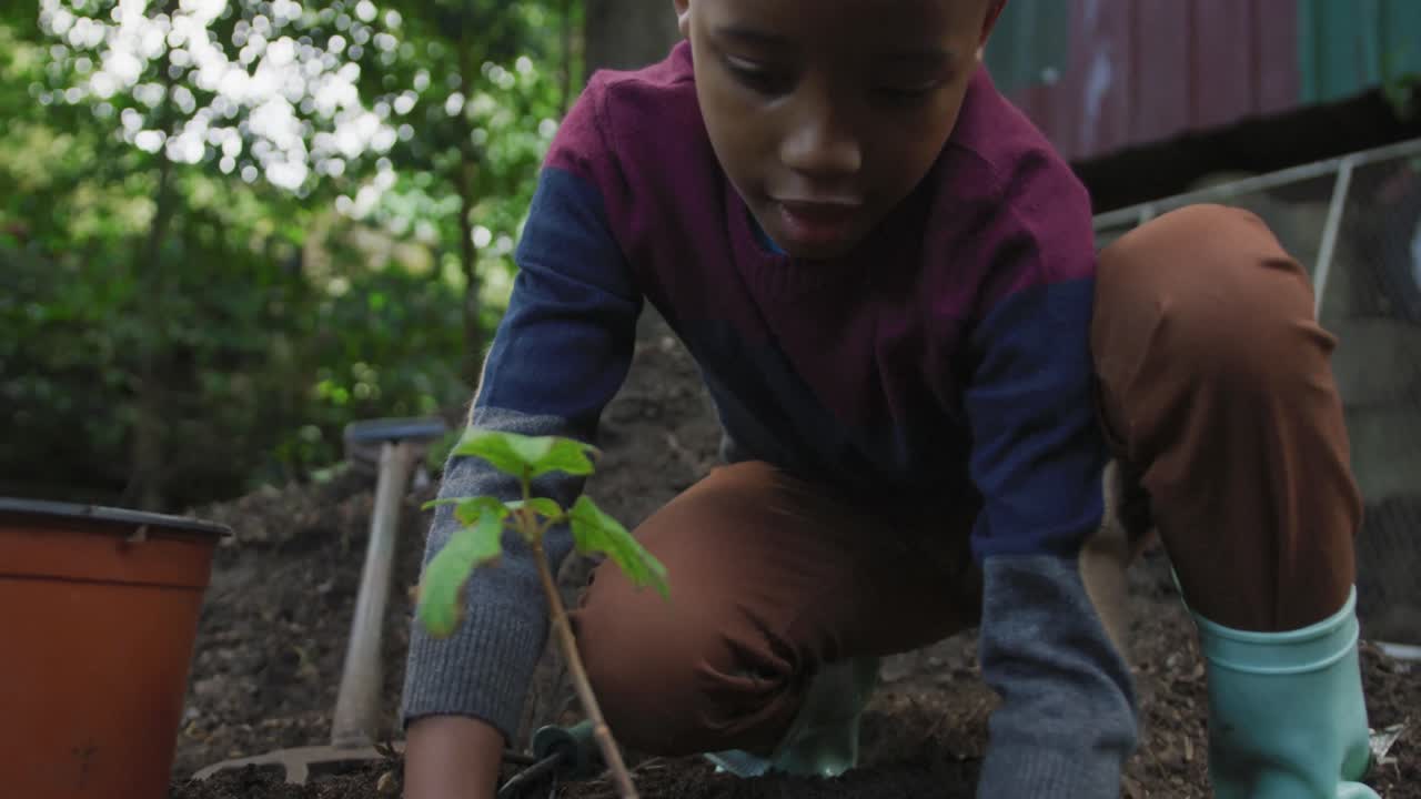 feliz niño afroamericano plantando una planta en el jardín