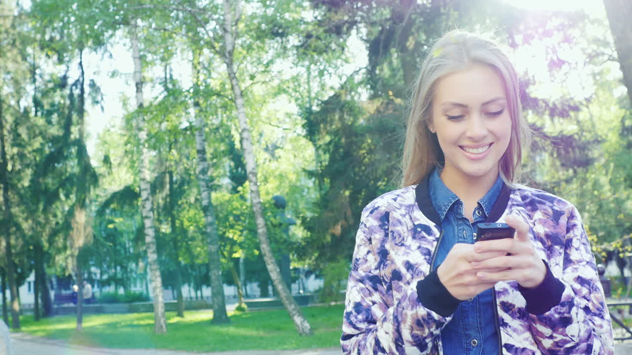 Attractive Woman Enjoying Smart Phone In A City Park The Sun Shines On It And Gives Beautiful Reflec