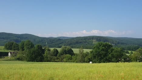 view of green meadow and hills in the background through the bus window while driving