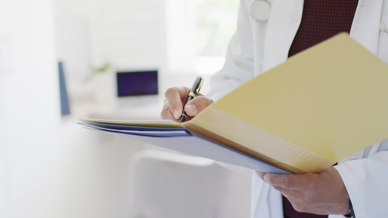 video de la sección media de un hombre biracial escribiendo notas en el archivo del paciente