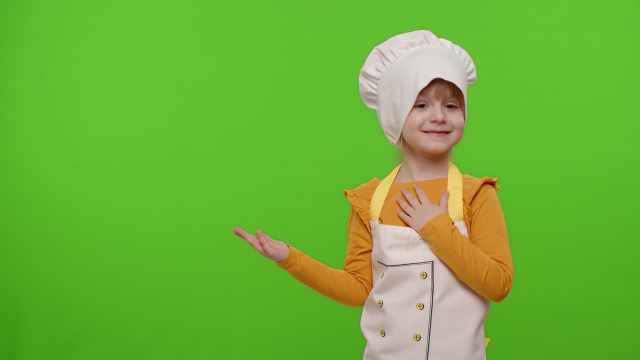 Child girl dressed cook chef baker in apron pointing at left on blank space on chroma key background