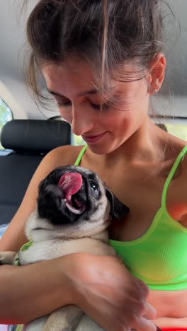 woman cuddling a pug puppy in a car