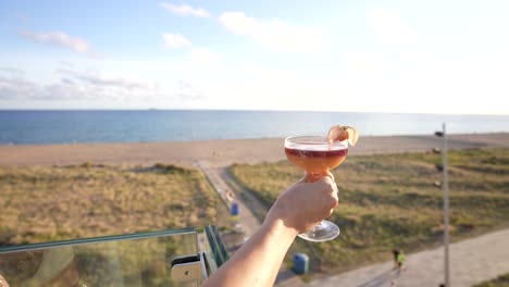 Cocktail-Auf-Einer-Terrasse,-Gehalten-Von-Einer-Frau-Mit-Wunderschöner-Und-Atemberaubender-Aussicht-Auf-Die-Landschaft-Auf-Dem-Meer-In-Einer-Bar-Auf-Dem-Dach