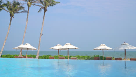 umbrella-with-bed-pool-around-swimming-pool-with-ocean-sea-background---holiday-and-vacation-concept